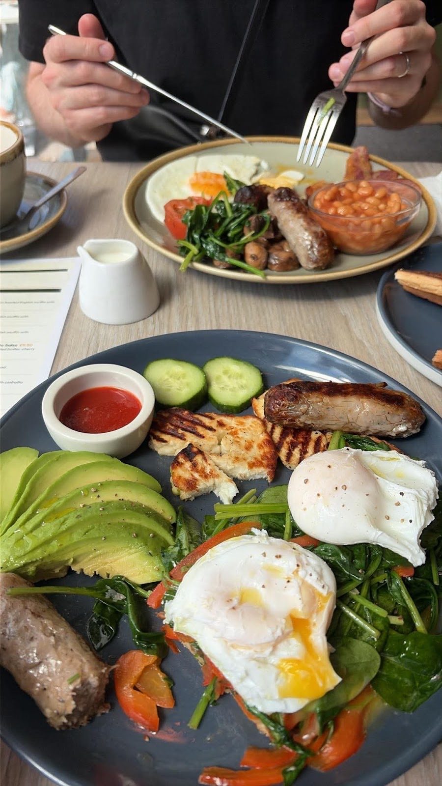 Two brunch plates on a table at Fields with a diner cutting into a cooked breakfast