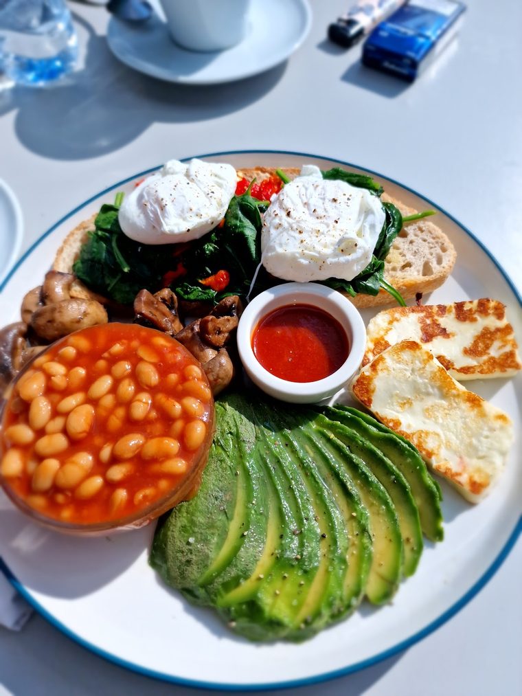 A plate of poached eggs, spinach, mushrooms, beans, halloumi and fanned avocado from above