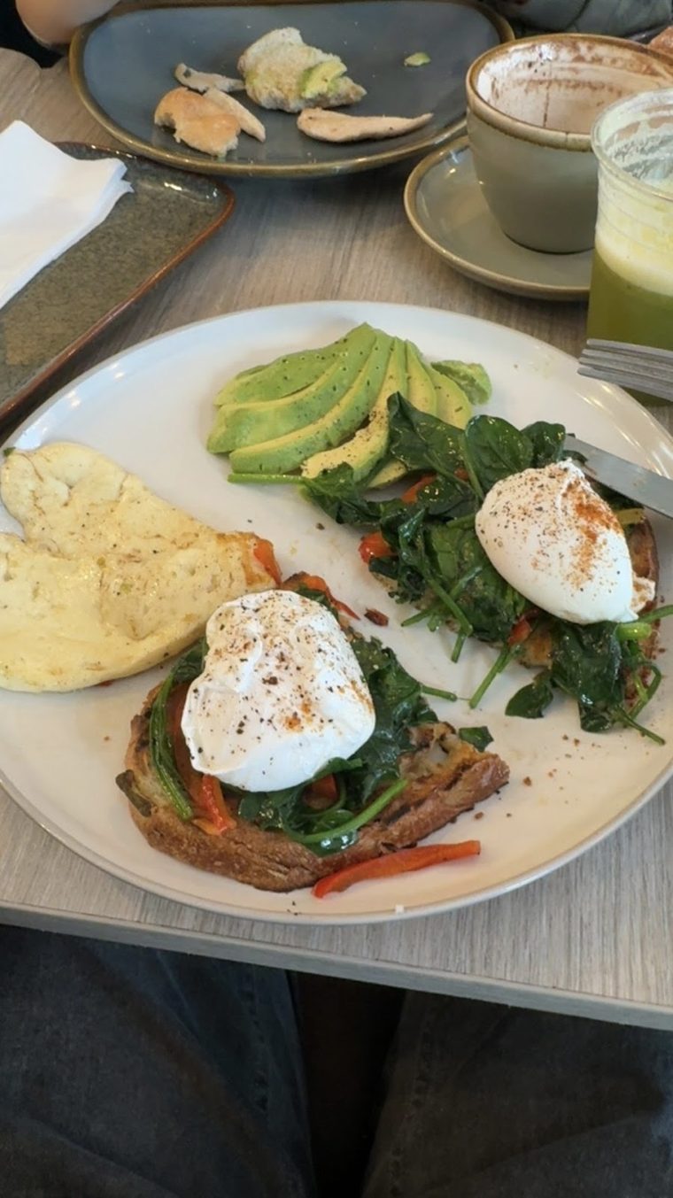 Poached eggs on toast with spinach and avocado, with coffee and a green juice behind