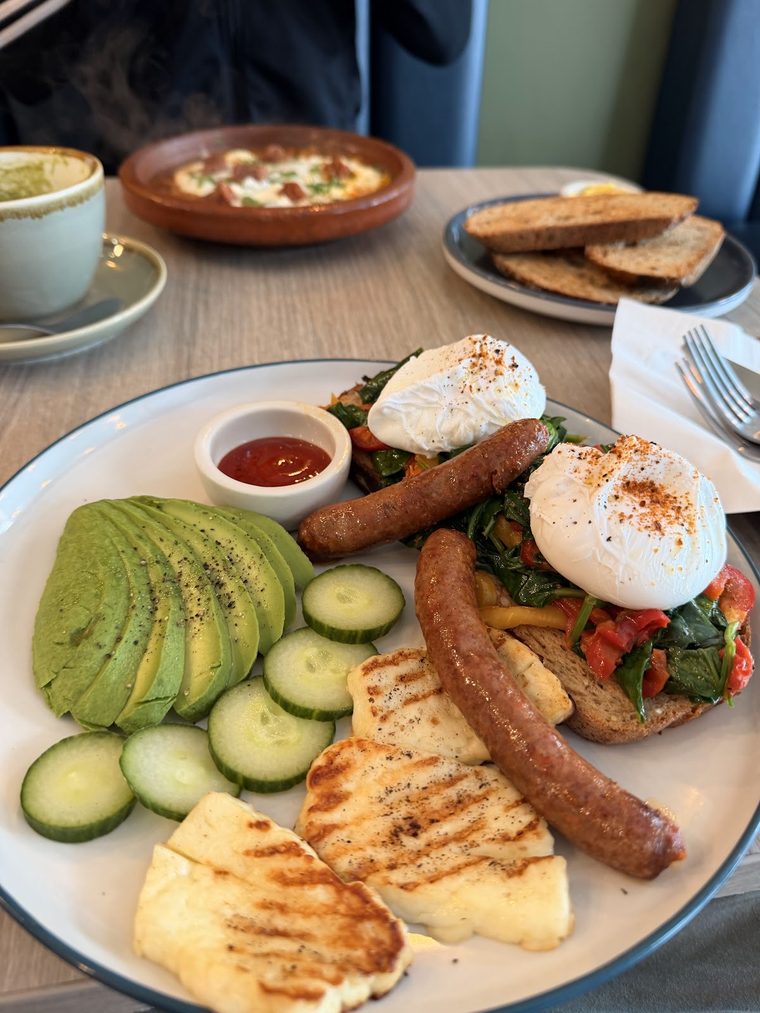 A large brunch plate of poached egg, sausage, halloumi, avocado and cucumber
